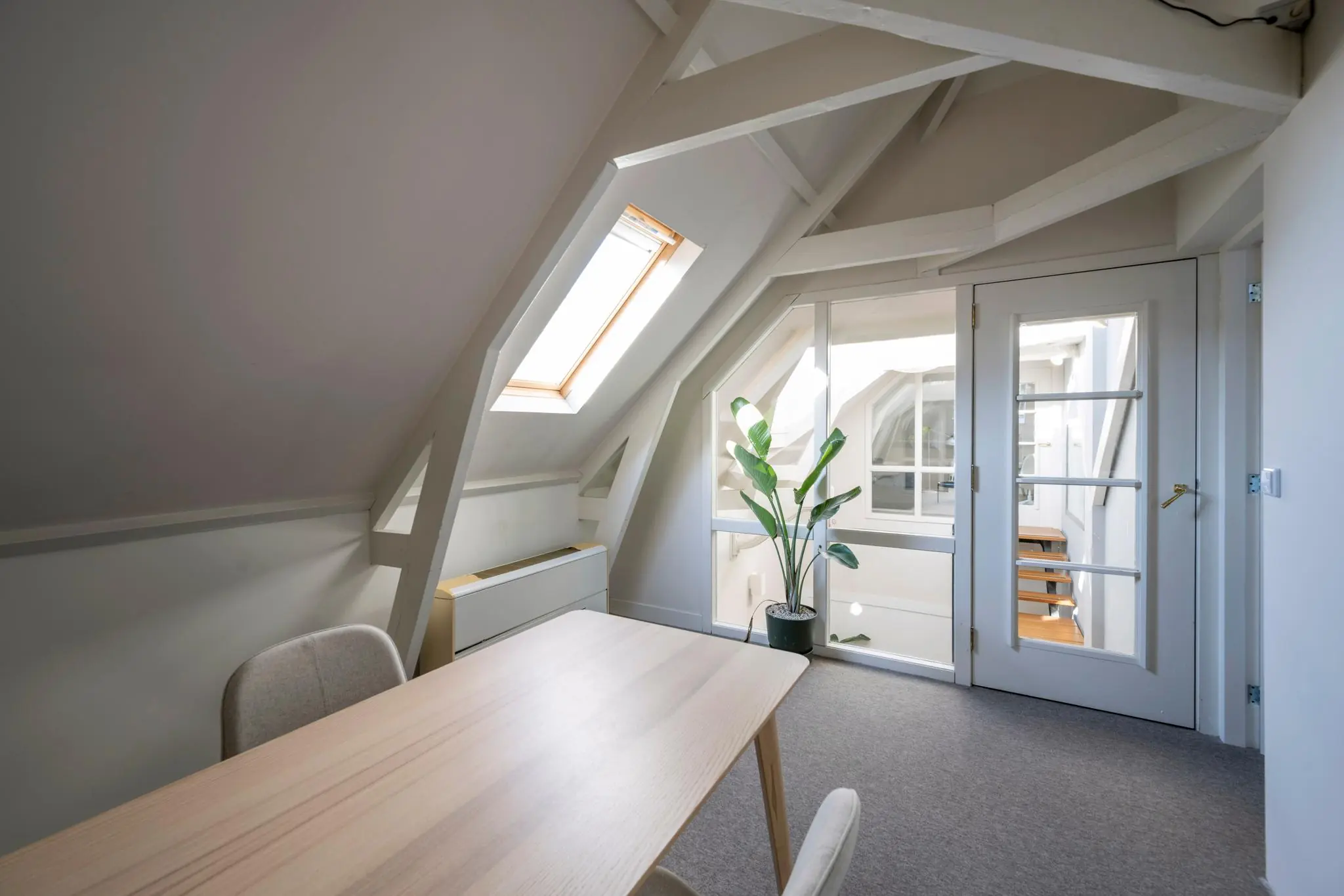 Licht en modern ingericht zolderkantoor aan de Prof. Tulpstraat met dakraam, houten tafel en glazen deur.